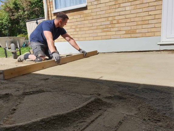 A worker smoothing out a freshly poured concrete driveway.