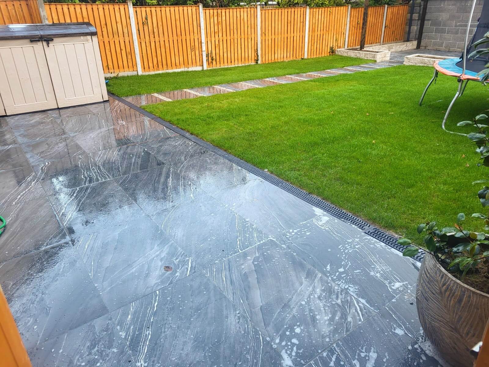 A glossy black stone patio next to a lush green lawn.